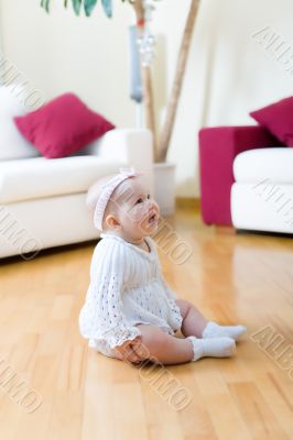 Happy eight month old baby girl seated on a hardwood floor