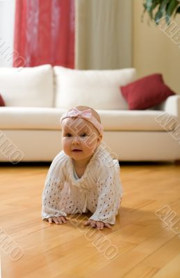 Happy eight month old baby girl crawling on a hardwood floor