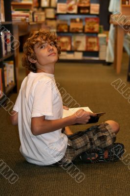 young teen boy sitting in bookstore reading