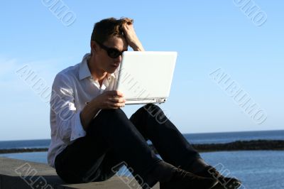 Young man with laptop at the coast sea