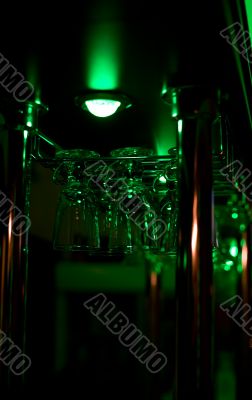 Glasses hang above a bar in green lighting