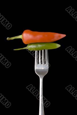 Red and green peppers on a silver for against a black background