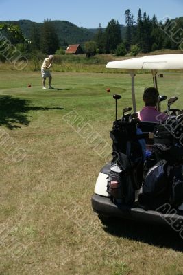 Woman in golf cart and woman teeing off