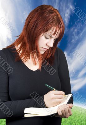 Cute redhead writing in her notebook or diary