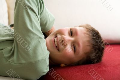 Happy teenager lie on red sofa at home