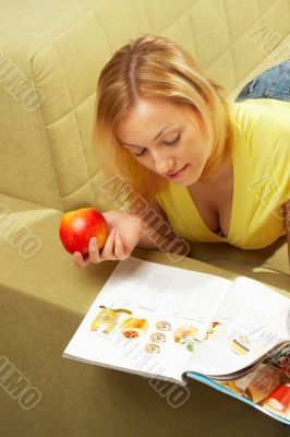 The girl lays on a sofa, reads the magazine