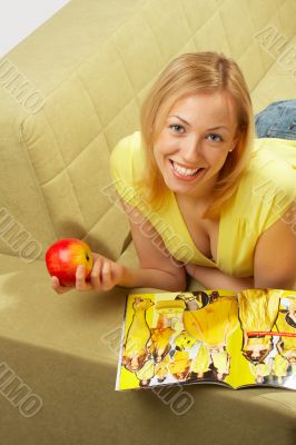 The girl lays on a sofa, reads &amp; smiles