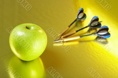 Apple and the darts laying on a golden background