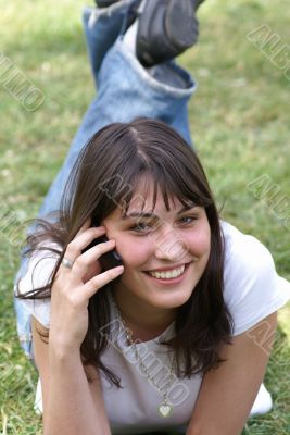 Smiling girl in a park with sell phone