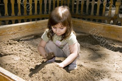 Child girl plaing at sand-box in summer park