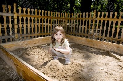 Child girl plaing at wood sand-box in summer park