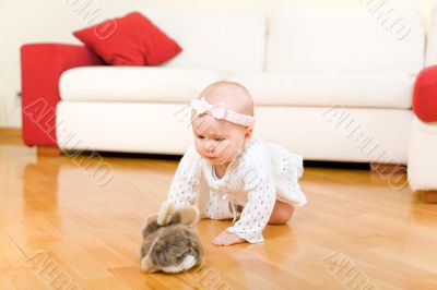 Happy eight month old baby girl crawling to rabbit toy