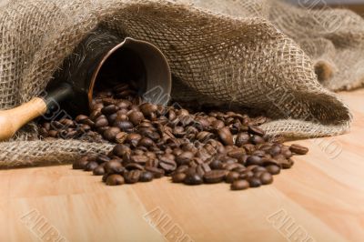 Sackcloth bag with cezve and roasted coffee beans on table