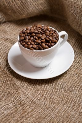 Cup with freshly roasted coffee beans on sackcloth