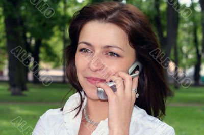young woman is talking by mobile phone in a park