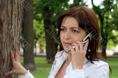 young woman is talking by mobile phone in a park