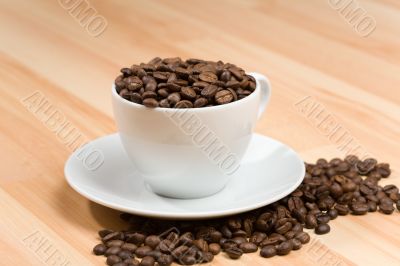 Cup with freshly roasted coffee beans on hardwood floor