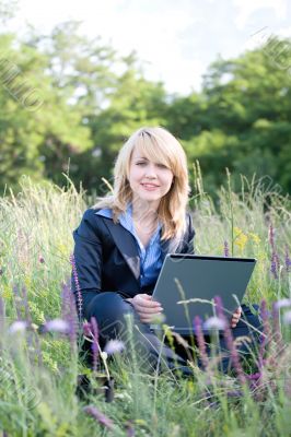 Businesswoman sitting on grass with laptop