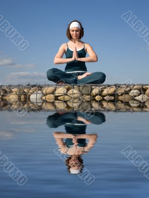 A woman doing yoga on a stone above  water