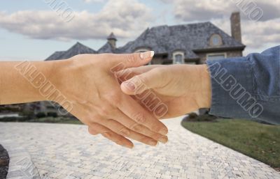 Man and woman shaking hands in front of a new house.