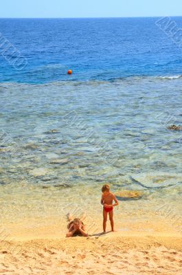 ma and son playing on beach on background blue sky