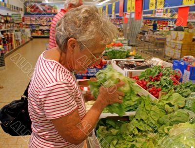Old woman buys salad in a supermarket