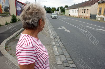 An old woman waiting for car on a road.