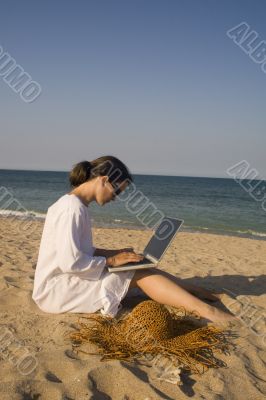 Woman sitting on beach with laptop