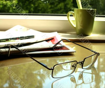The eyeglasses, the newspaper  and the green cup