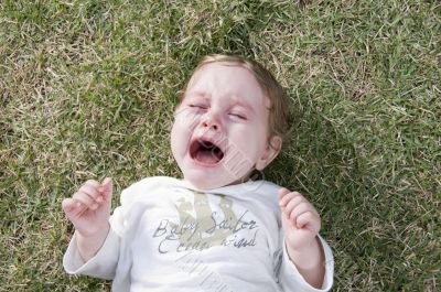 adorable child crying and lying in the garden