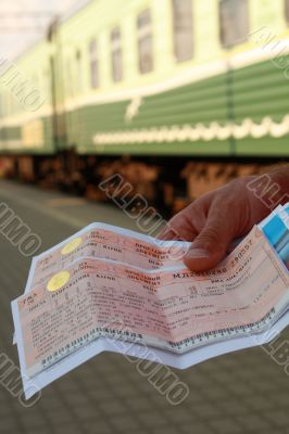 Green train at station in a hand two tickets