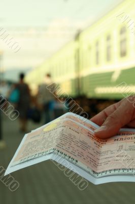 Green train at station in a hand two tickets