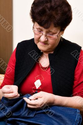 Grandmother sewing trousers on the couch