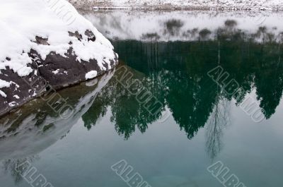 Big stone covered a snow in nonfreezing blue lake