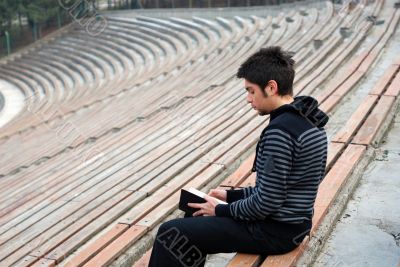 lonely man reading book in empty stadium