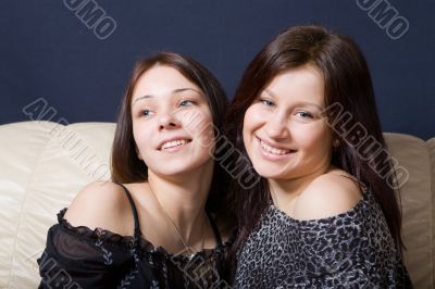 Two happy girls sit on a sofa