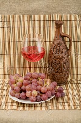 Ceramic bottle, grape and goblet on mat