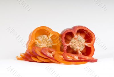 Cut orange and red sweet pepper showing seeds with slices on whi