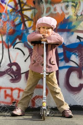 Cute little girl with scooter near graffiti wall