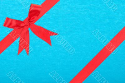 Red satin ribbon and bow gift box wrapping over blue paper backg