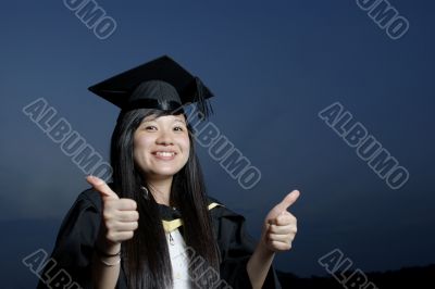 Smiling asian female graduate with thumbs up sign