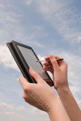 Hands hold electronic book reader against blue sky