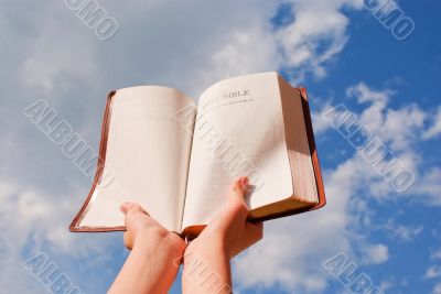 Hands hold the open Bible against blue sky