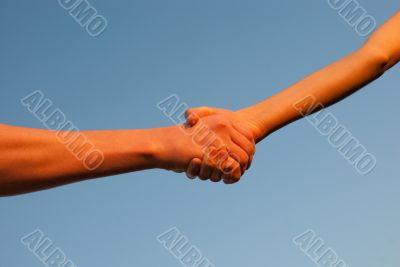 Hands shaking each other against blue sky