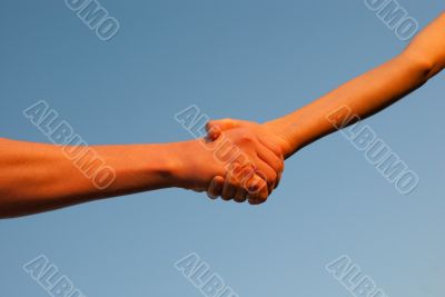 Hands shaking each other against blue sky Hands shaking each other against blue sky