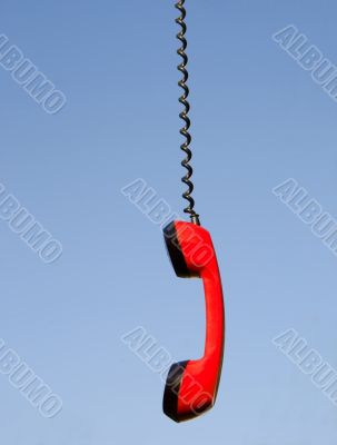Red phone handset hanging against blue sky
