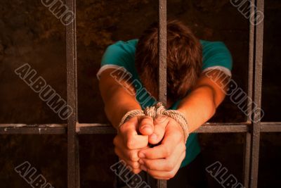 Man with hands tied with rope behind the bars