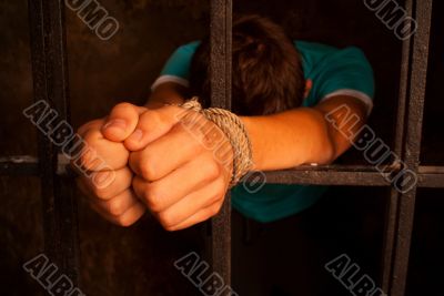 Man with hands tied with rope behind the bars