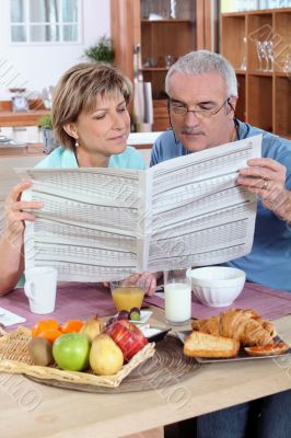 Couple reading the newspaper over breakfast Couple reading the newspaper over breakfast