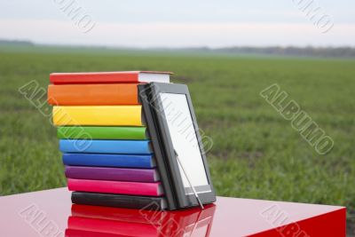 Stack of colorful books and electronic book reader outdoors